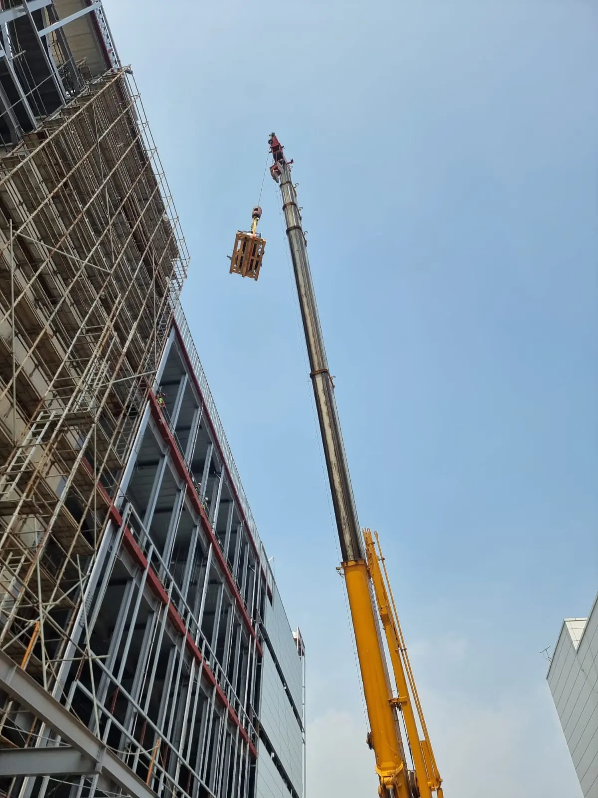 Crane mengangkat muatan di samping bangunan rangka baja dengan scaffolding di lokasi PTJ Hyundai LG Battery